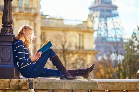 young woman reading book on a city wall in France, eiffel tower in background