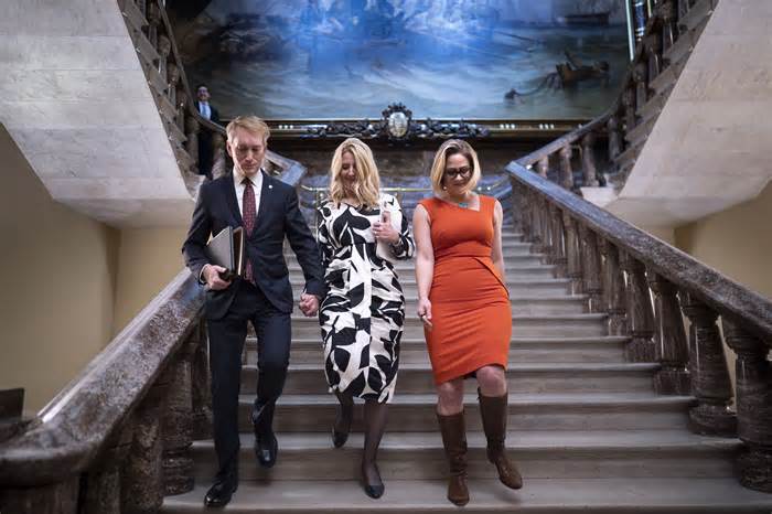 Sen. James Lankford, R-Okla., left, the lead GOP negotiator on a border-foreign aid package, holds hands with his wife Cindy Lankford, center, joined at right by Sen. Kyrsten Sinema, I-Ariz., who has been central to Senate border security talks, during procedural votes, at the Capitol in Washington, Wednesday, Feb. 7, 2024. Senate Republicans have blocked the bipartisan border package, scuttling months of negotiations between the two parties on legislation intended to cut down record numbers of illegal border crossings. (AP Photo/J. Scott Applewhite)