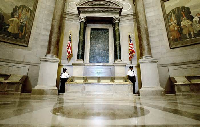 FILE - Guards stand next to the U.S. Constitution in the newly renovated Rotunda of the National Archives in Washington, Sept. 16, 2003, during a media tour. The National Archives building and galleries were evacuated Wednesday afternoon, Feb. 14, 2024, after two protestors dumped red powder on the protective casing around the U.S. Constitution. (AP Photo/Ron Edmonds)