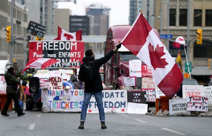 FILE - A protester waves a Canadian flag in front of parked vehicles at a protest against COVID-19 measures that has grown into a broader anti-government protest, in Ottawa, Ontario, Feb. 11, 2022. In a decision released Tuesday, Jan. 23, 2024, a Canadian judge ruled that the government’s use of the Emergencies Act to quell weeks of protests by truckers and others angry over COVID-19 restrictions in 2022 was unreasonable and unconstitutional. (Justin Tang/The Canadian Press via AP, File)