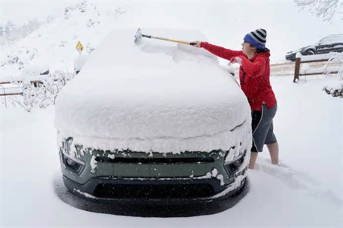 A person clears their car of snow to go to work, in Provo, Utah, on Feb. 22, 2023. - 29 US states are under winter weather alerts as people brace for a winter storm expected to bring heavy snow, wind, and freezing temperatures from the west to the east coast.