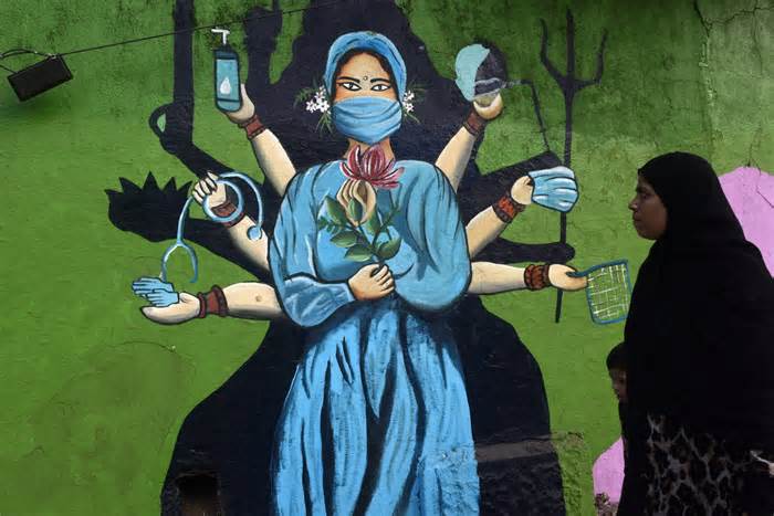 A Muslim woman is walking past a mural painting of a face wearing masks amid a sudden surge of the JN.1 coronavirus in Mumbai, India, on Jan. 11. The variant is dominant globally, and its descendants appear poised to take off.