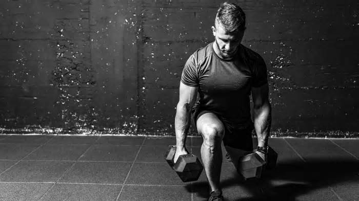 Dumbbell legs training, Young strong fit muscular sweaty man with big muscles strength cross workout training with dumbbells weights in the gym dark image with shadows real people black and white