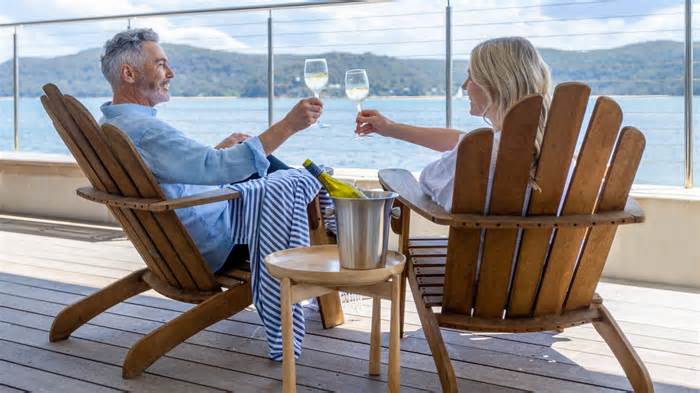 happy retired couple cheers wine glasses outdoor deck_iStock-1471508047