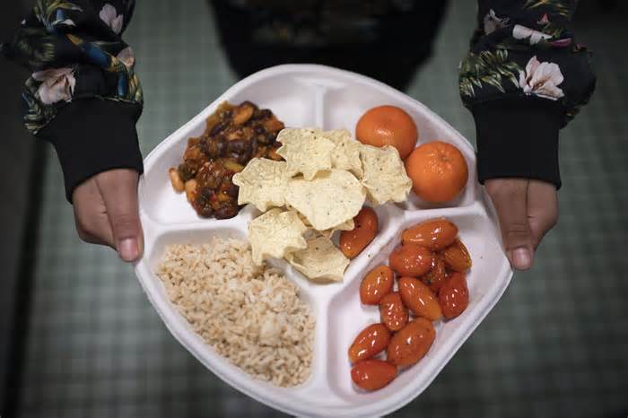 FILE - A seventh grader carries her plate which consists of three bean chili, rice, mandarins, cherry tomatoes and baked chips during her lunch break at a public school in the Brooklyn borough of New York on Friday, Feb. 10, 2023. Experts agree that the urgency of climate change and the demands of a surging global population call for an overhaul of how humans get their protein. (AP Photo/Wong Maye-E, File)