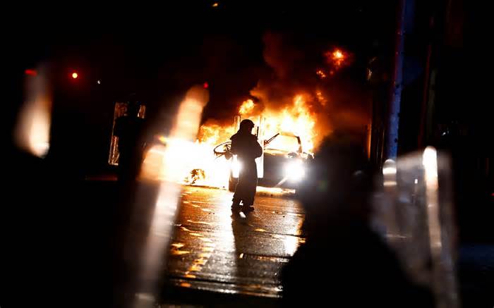 Riot police walk next to a burning police vehicle, Dublin, Ireland