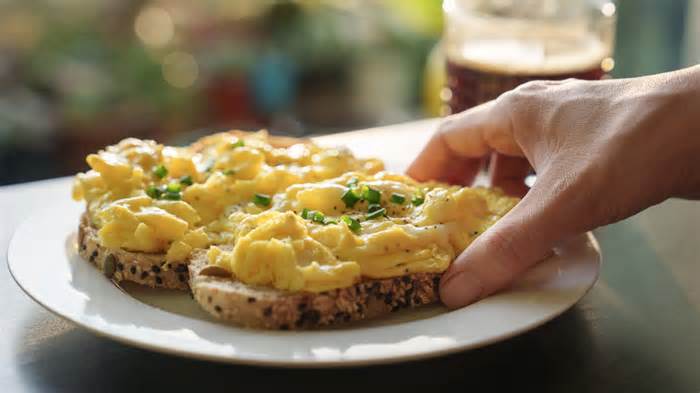 Person reaching for scrambled eggs on toast