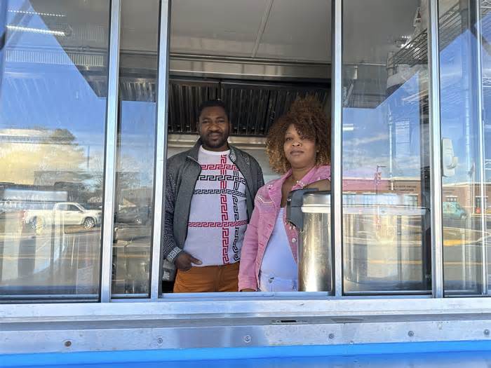 Theslet Benoir and Clemene Bastien stand at the window of their Eben-Ezer Haitian food truck in Parksley, Va., on Wednesday, Jan. 24, 2024. The married couple is suing the town in federal court over allegations that their food truck was forced to close. The couple also says a town councilman cut the mobile kitchen's water line and screamed, 