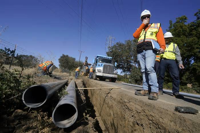 Paul Standen, senior director of underground regional delivery, second from right, and project manager Jeremy Schanaker, right, look on during a tour of a Pacific Gas and Electric crew burying power lines in Vacaville, Calif., Wednesday, Oct. 11, 2023. (AP Photo/Jeff Chiu)