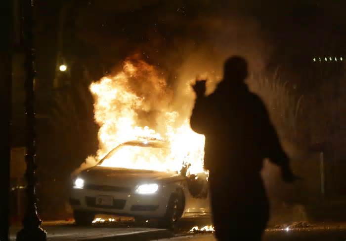 FILE - A police car is set on fire amid protests that followed the announcement that a grand jury had declined to indict Ferguson police officer Darren Wilson in the death of Michael Brown, Nov. 24, 2014, in Ferguson, Mo. On Tuesday, Jan. 3, 2024, a St. Louis-based public interest law firm announced that the city of Florissant, Mo., will pay nearly $3 million to settle a so-called debtor's prison lawsuit that accused Florissant and six other St. Louis suburbs of violating the constitutional rights of residents by jailing them and forcing them to pay fines and fees amounting to millions of dollars. Florissant was among several St. Louis County cities whose policing and court practices fell under scrutiny after the fatal police shooting of Brown. (AP Photo/Charlie Riedel, File)
