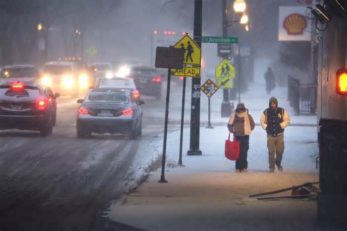 Pedestrians navigate a snow-covered sidewalk