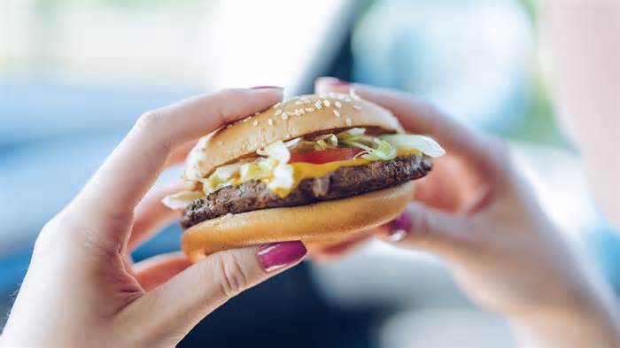 woman holding fast food cheeseburger interior car_iStock-1030408822