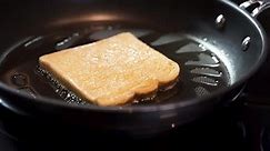 tilt up from black stove top to french toast frying in a pan, french toast is then flipped over by a