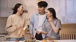 無料 ストック動画 - 3 人の日本人の友人がキッチン カウンターの周りで日本食を食べ、カメラを見て笑顔で ok サインをしている