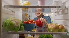 Beautiful Young Woman Opens Fridge Door, Looks inside Takes out Vegetables. Woman Preparing Healthy Meal Using Groceries. Point of View POV from Inside of the Kitchen Refrigerator full of Healthy Food