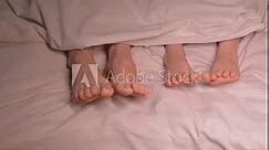dancing legs of boy son child and mother female foot under blanket on sheet in the evening. Happy baby kid girl daughter and woman mom wiggling bare feet in bed in the bedroom