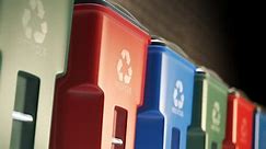 Colorful, plastic garbage bins, with recycle logo on the front, stacked in a row against a brick wall in an endless, loop. Symbol of recycling, waste sorting, ecology and saving the environment.