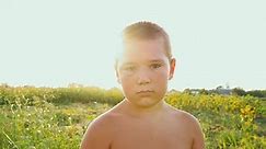 Portrait of a chubby boy with a black eye on the background of a green field, a sad child with a naked torso and a bruise on his face