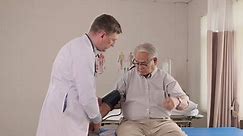 Caucasian male doctor in uniform health checks illness senior patient, blood pressure by measure gauge in emergency room bed at hospital ward, elderly medical clinic, painful examination consultant.