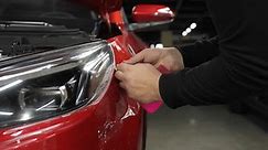 The master applies vinyl film to the headlight of a red car.