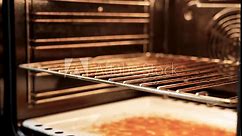 Woman cleaning oven after cooking a fatty dish in the kitchen, close-up. Hands pulls out baking tray with fat. Kitchen cleaning service and housekeeping. Selective focus, 4k.