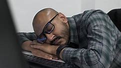 Premium stock video - A young indian entrepreneur slumped over an office desk, asleep in front of his computer exhausted from working late putting together his business proposal